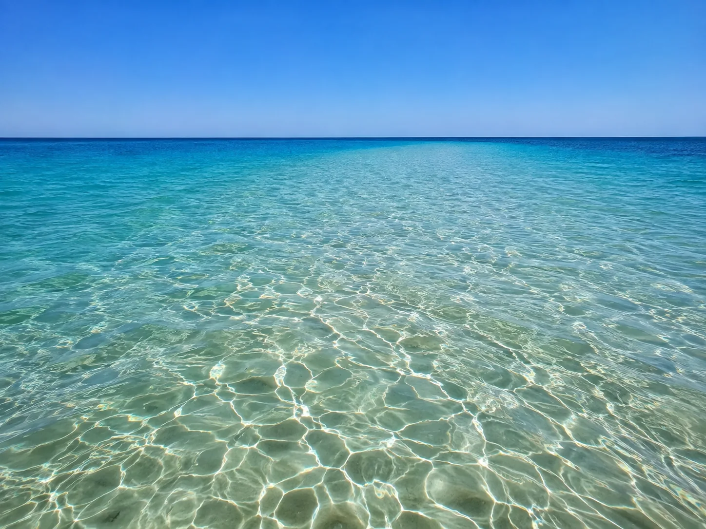 Clear shallow water over a pale sand bottom running out to a bar where the colour changes from green to deep blue, of the kind you stand up in at the Stingray City sandbar